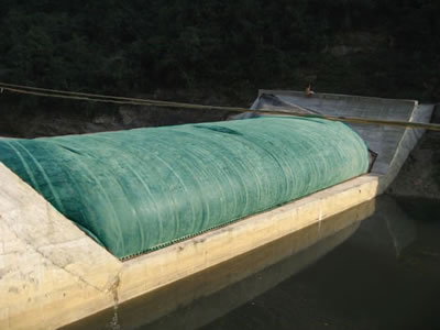 A blue inclined water inflatable rubber dam is on the concrete foundation and the water level is low.