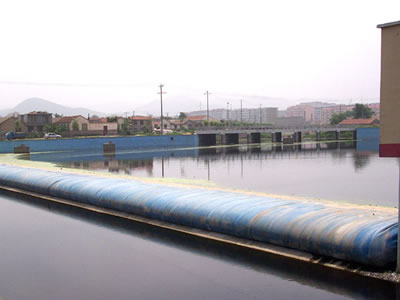 A blue pillow-like water inflatable rubber dam is on the concrete foundation and the water level is low.