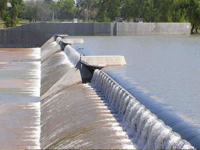 A black bookend rubber dam is on the top of a slope and there are several piers above the dam.