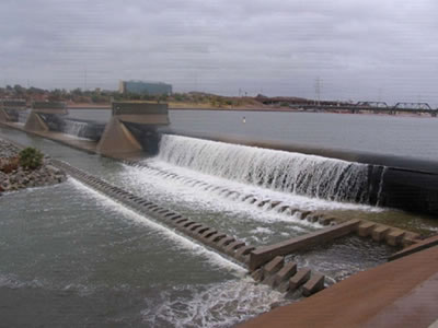 Water is flowing through long span bookend rubber dam and there are several piers above the dam.