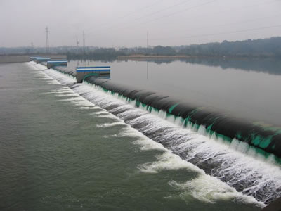 A green water inflatable rubber dam with black protective layer has overflow and many piers.
