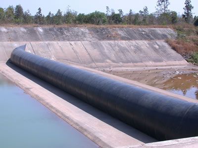 Black air inflatable rubber dam is installed on concrete foundation, upstream and downstream has water.