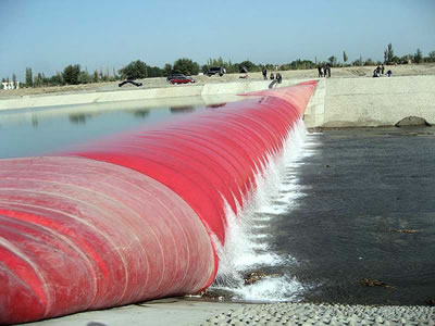 Water overflow flows the top of red air inflatable rubber dam.