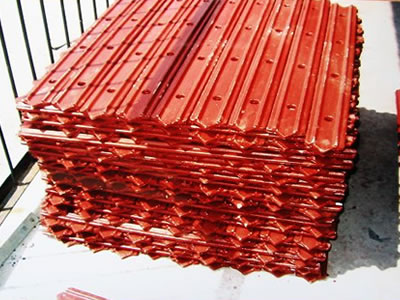 Many pointed end clamping plates with red paint are placed on ground neatly.