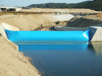Sky-blue air inflatable rubber dam is installed on concrete foundation which one side has water.